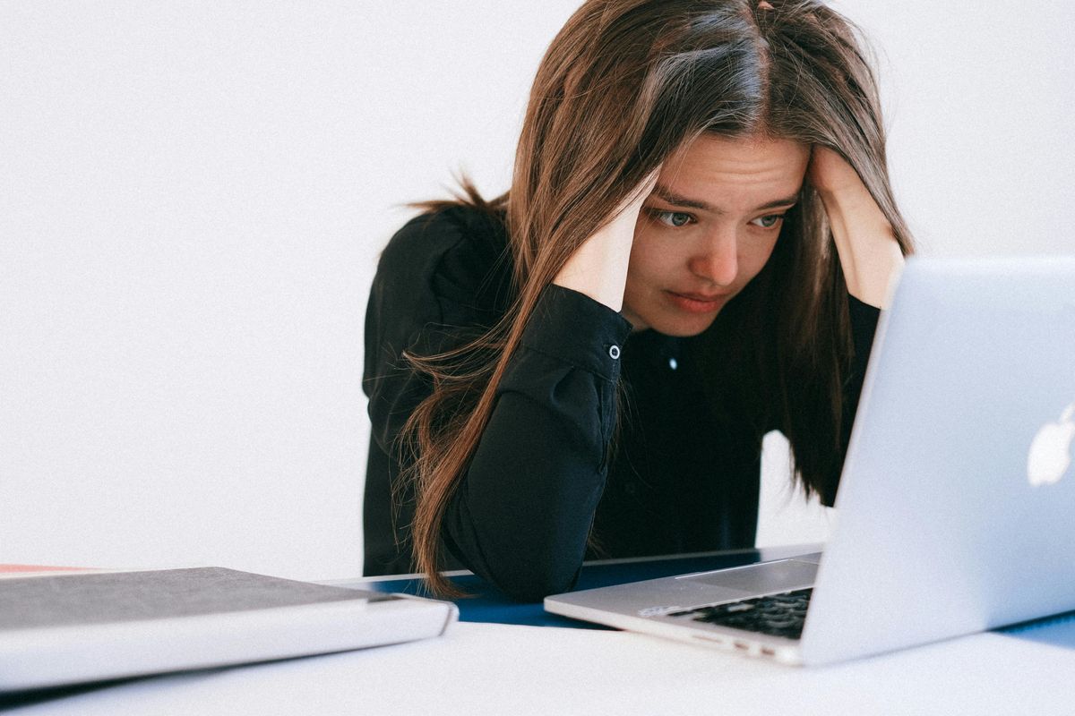 Eine junge Frau, den Kopf in den Händen, liest eine schlechte Nachricht auf ihrem Laptop